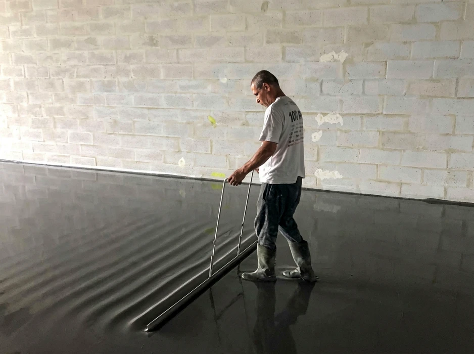 Ouvrier en intérieur appliquant une chape liquide autonivelante sombre sur un sol
