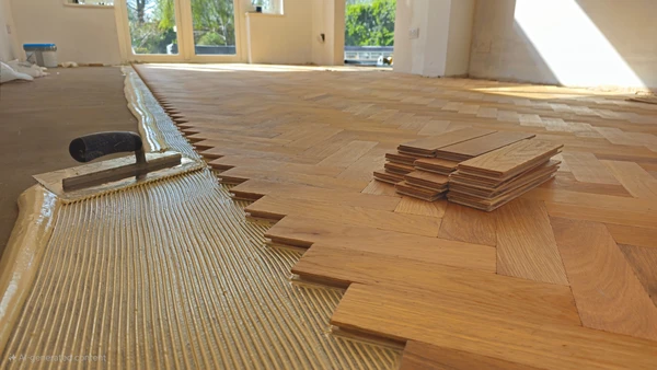 Photographie en gros plan d'un chapiste professionnel en &eacute;quipement de travail (gilet de s&eacute;curit&eacute;, bottes de protection) installant un syst&egrave;me de plancher chauffant sur une surface de chantier int&eacute;rieur. L'artisan positionne et fixe les &eacute;l&eacute;ments chauffants (tubes de pex ou tapis chauffants visibles) sur une surface pr&eacute;par&eacute;e, potentiellement &agrave; proximit&eacute; d'une pompe de distribution ou d'un syst&egrave;me de contr&ocirc;le du plancher chauffant. On doit clairement voir les tubes ou &eacute;l&eacute;ments chauffants en cours d'installation, les fixations, et le contraste entre les zones pr&eacute;par&eacute;es et les zones non encore &eacute;quip&eacute;es. L'arri&egrave;re-plan montre un chantier int&eacute;rieur avec une structure de b&acirc;timent visible. La composition met en &eacute;vidence le professionnalisme, la technique d'installation pr&eacute;cise du syst&egrave;me de chauffage int&eacute;gr&eacute; et l'expertise requise pour cette installation sp&eacute;cialis&eacute;e.