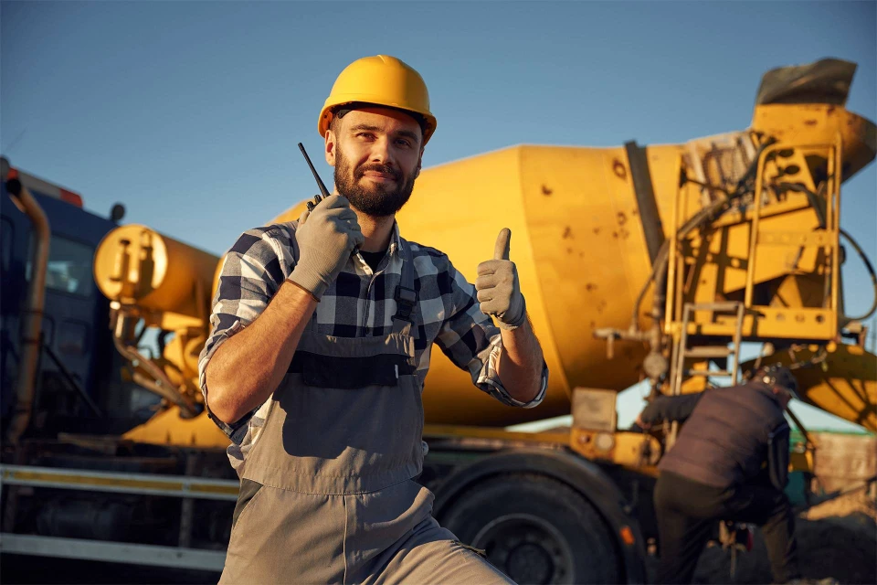 Photographie d'un chantier de revêtement de sol montrant différentes étapes du travail : au premier plan, un ouvrier en tenue professionnelle appliquant une résine époxy ou un revêtement de sol avec un outil spécialisé ; en arrière-plan, les phases antérieures visibles incluant une chape ciment en préparation et des matériaux de base. L'image doit montrer la progression du travail de sol du support brut au revêtement fini, illustrant ainsi la chaîne complète de travaux prise en charge par l'entreprise. Éclairage naturel ou professionnel mettant en valeur les détails du chantier et la professionnalité de l'intervention.