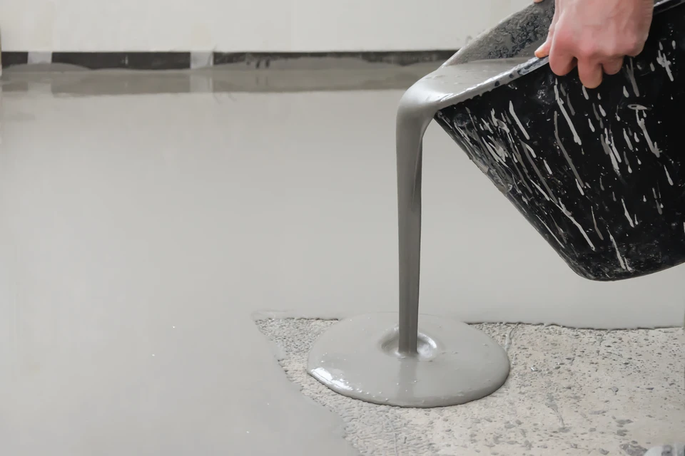 Ouvrier en tenue rouge appliquant une chape liquide sur un plancher chauffant à l'intérieur d'un bâtiment en construction