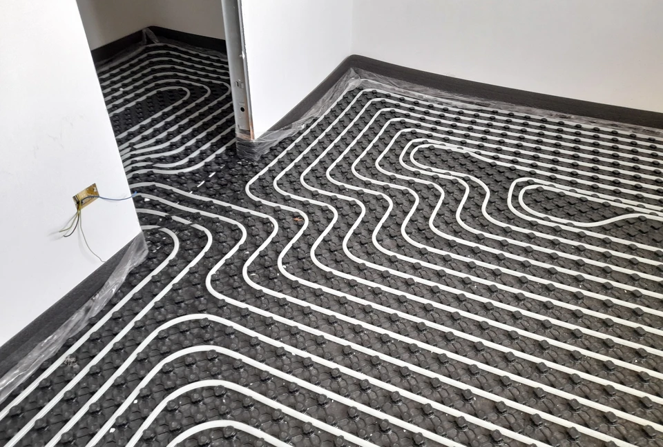 Ouvrier posant carrelage sur sol intérieur, mains gantées appliquant carreaux gris sur mortier-colle